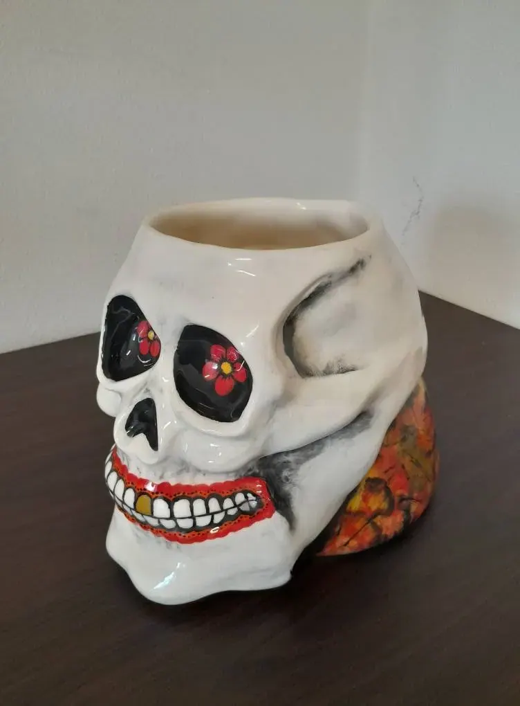 A white ceramic skull pot with red painted eyes