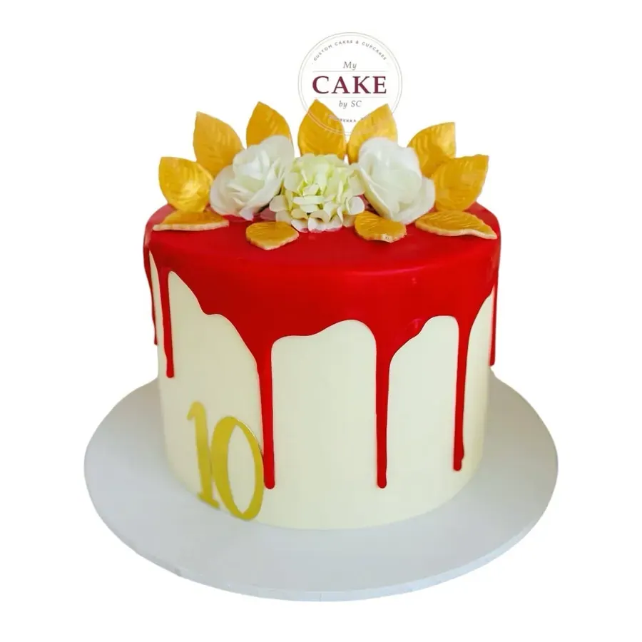 A white cake with a red drip and gold petals