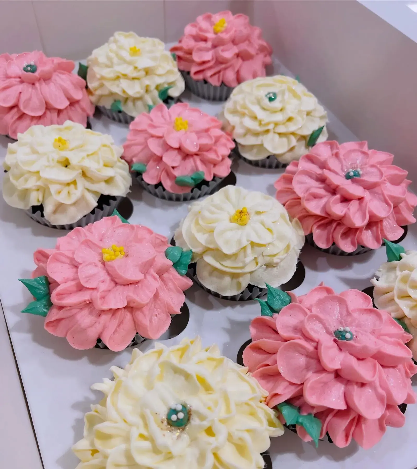 A tray of pink and cream flower cupcakes